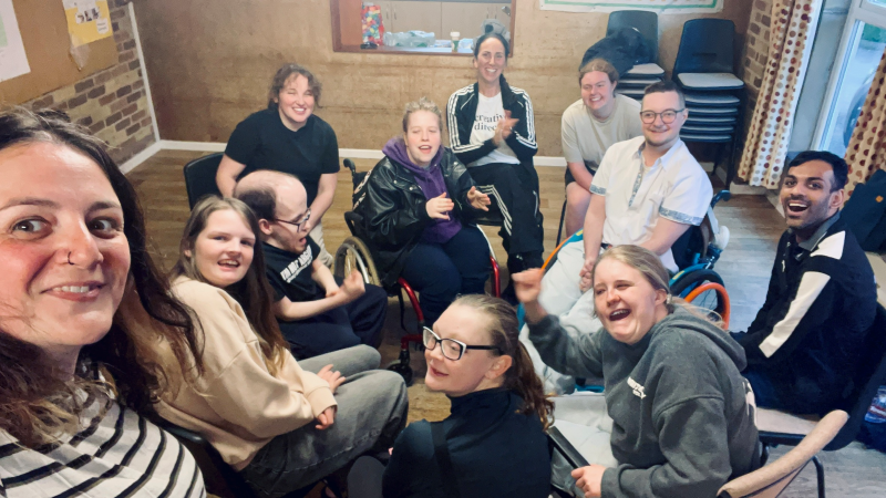 A group of young disabled activists and Grapevine community organisers gather for a CYA selfie inside a community meeting room.