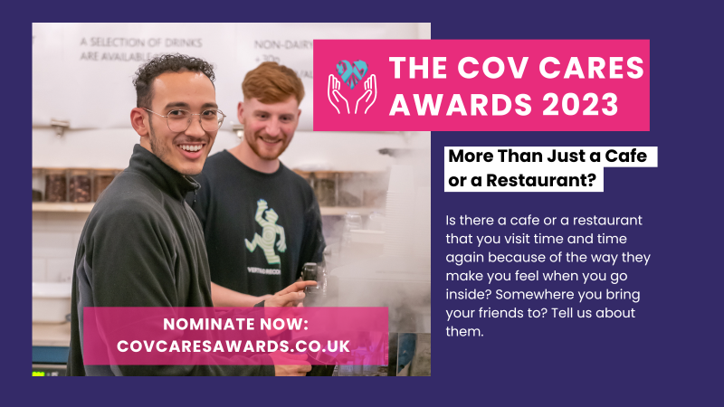 Two young men turn to smile at the camera as they work in a professional kitchen.