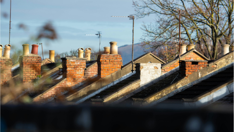 Photo of brick chimneys, rooftops and aerials along a suburban street against a blue winter sky. Credit: Richard Bell on Unplash.