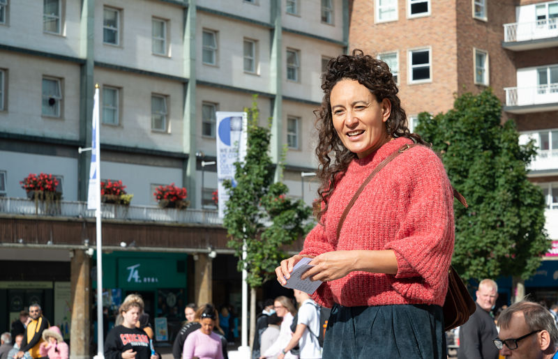 A woman in a red jumper stands before the crowd in Broadgate to share her story