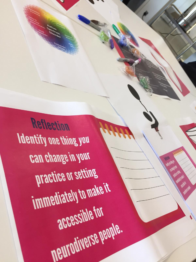 Pieces of paper are laid out on a table at the briefing session with one on pink paper asking what immediate change providers could make to create a more accessible setting for neurodiverse young people.