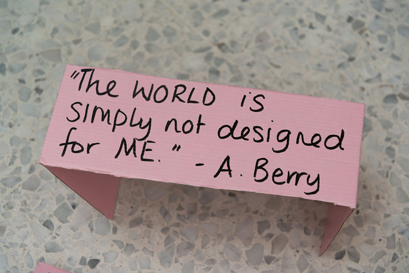 Black words written on pink paper and laid on the floor read "The world is simply not designed for me" A.Berry