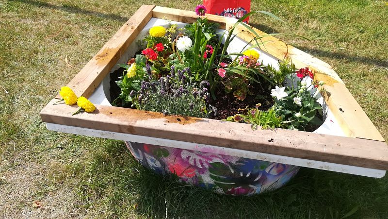 A planted recycled bathtub filled with flowers and decorated with paint