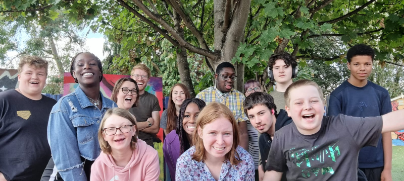 A large group of Teenviners and staff stand in front of a tree for a group photo. They are all smiling, some are cheering.