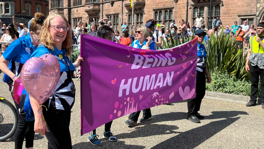 City of Culture hosts dressed in Coventry Blue t-shirts hold a purple Being Human banner at the front of this section in the parade