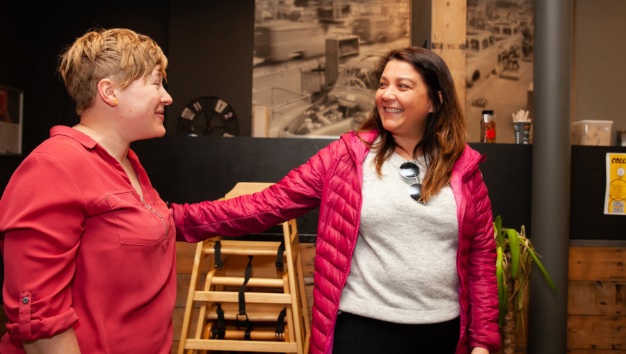 Two women greet each other warmly inside a coffee shop hosting Collaboration Station. The woman on the left with short blonde hair and a peach coloured shirt is Gemma from Connecting For Good Cov. The text on the image reads: "We are open as a team that we don’t have the answers, we don't always get it right and we can’t do it alone."