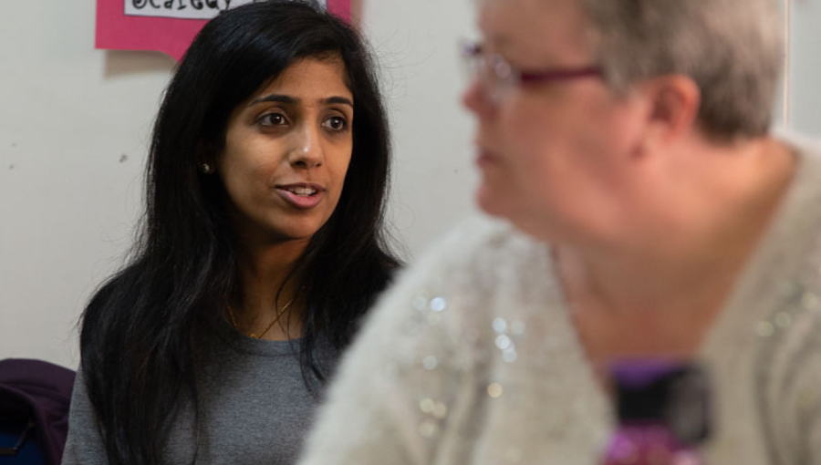 An asian woman with long dark hair sits behind a white woman in a training session run by the Health Team. Cut out red scaredy pants can be seen hanging on a washing live for an activity about feeling afraid to ask the right questions.