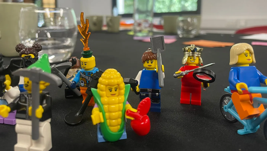 Lego figures using various tools on a table in a conference room.