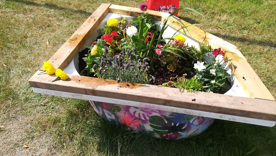 A planted recycled bathtub filled with flowers and decorated with paint