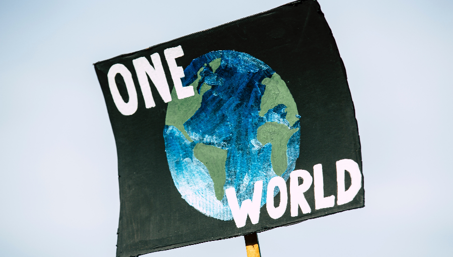 A placard is held aloft with a black background and Earth and words in white capital letters that say 'One World'.