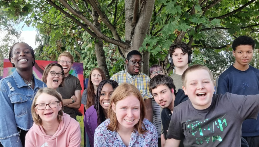 A large group of Teenviners and staff stand in front of a tree for a group photo. They are all smiling, some are cheering.