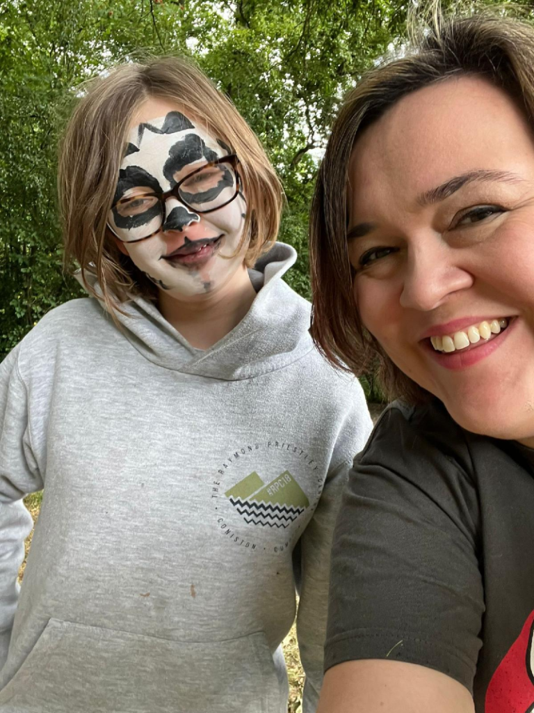 Sarah from Teenvine and young girl with her face painted in black and white smile at the camera as Sarah takes a selfie at the summer festival.