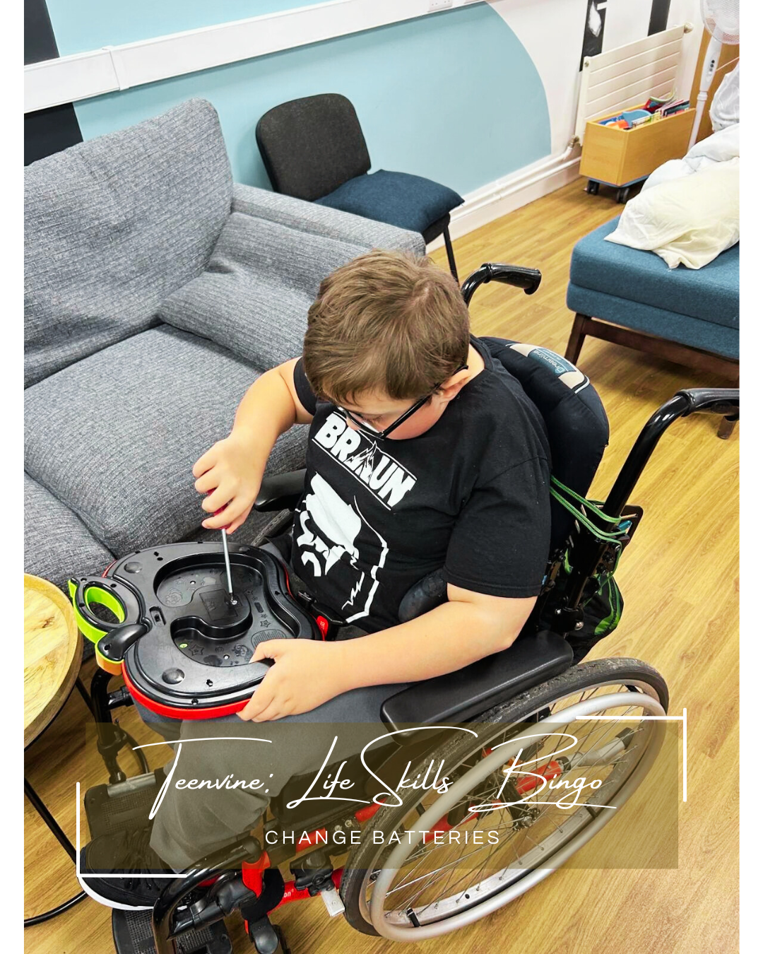 A white boy wearing a black t-shirt and using a wheelchair holds a screwdriver as he changes the batteries in a wall clock.
