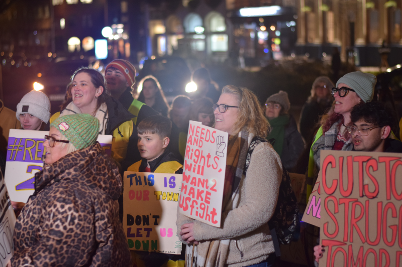 Demonstrators hold colourful placards and listen intently as someone's story is shared outside Coventry Council House.