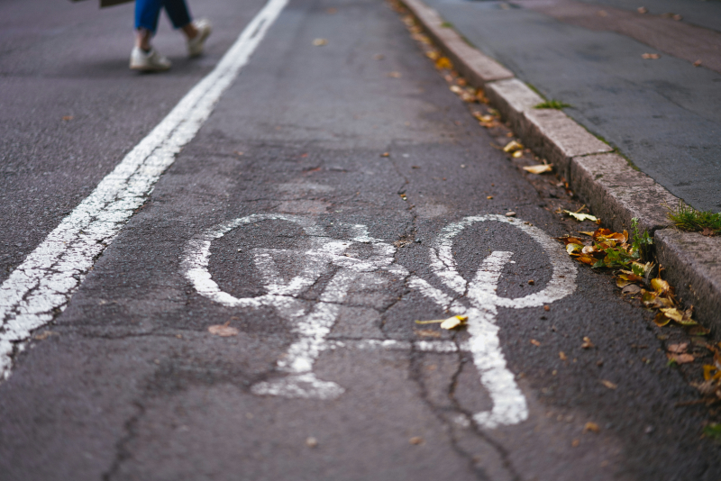 Photo of a painted cycle lane on a street with the pavement on one side and someone crossing the road on the other.