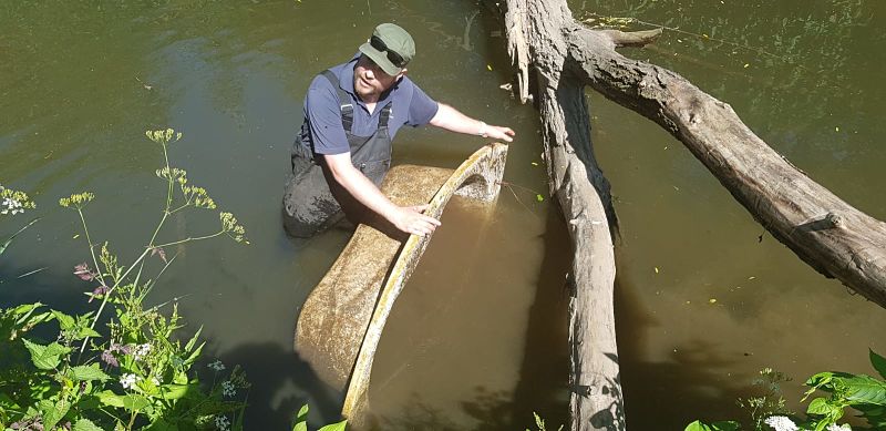 A man in waders pulls a bathtub from the River Sowe in Coventry