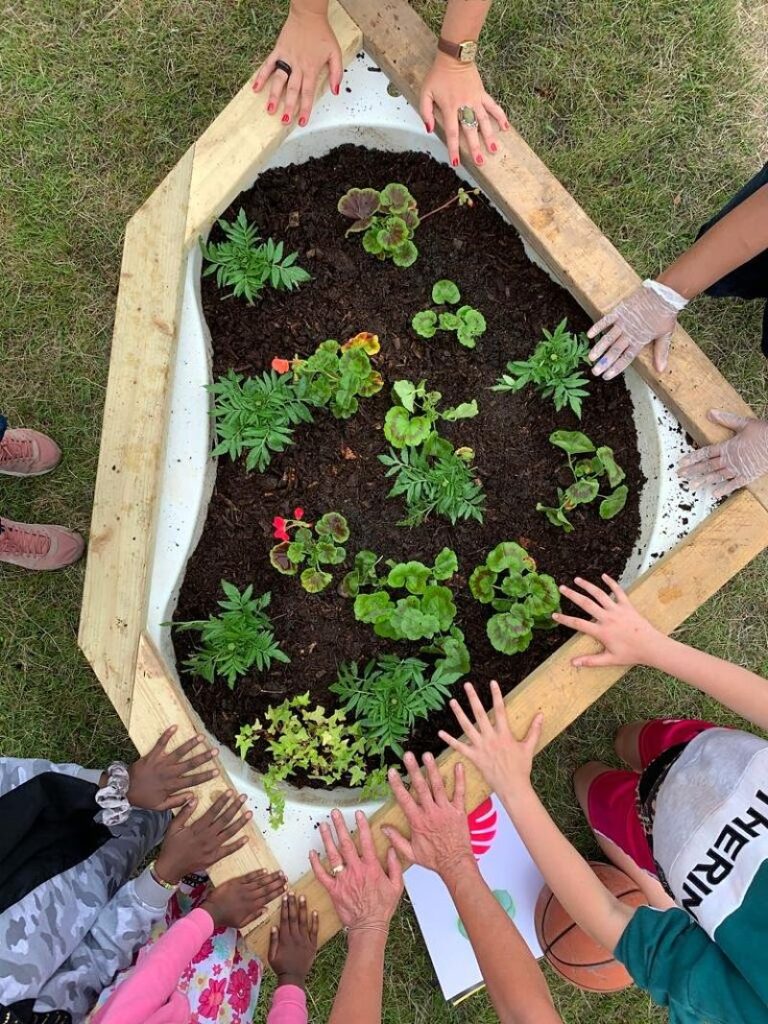 Different pairs of hands hold the edges of a painted recycled bathtub planter in Stoke Aldermoor, Coventry