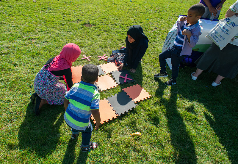 A group of women with children put a large foam mat jigsaw together on grass