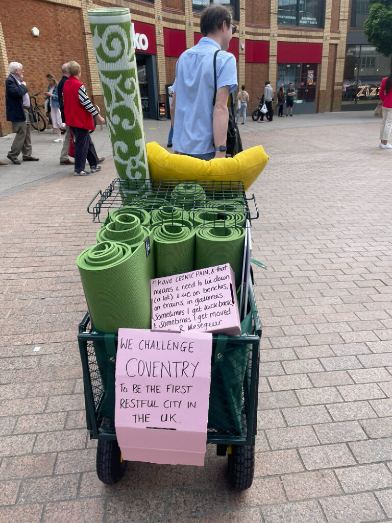 A trolley containing rolls of faux grass and handmade placards is pulled across Coventry city centre for a Grapevine parklet. 