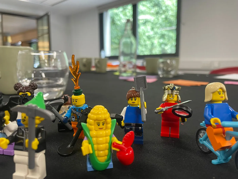 Lego figures using various tools on a table in a conference room.