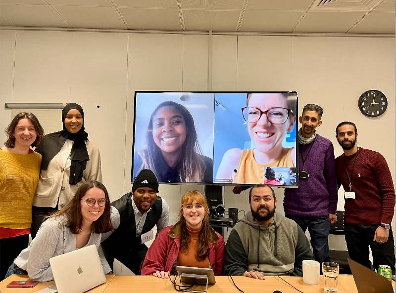 Eight people, plus two more on a big Zoom screen, smile for the camera as the panel gathers in London for a meeting.