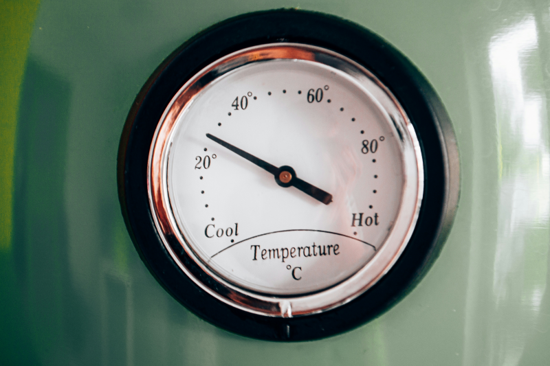 A weather barometer on a green wall with a gauge that points from cold to hot in degrees celsius.