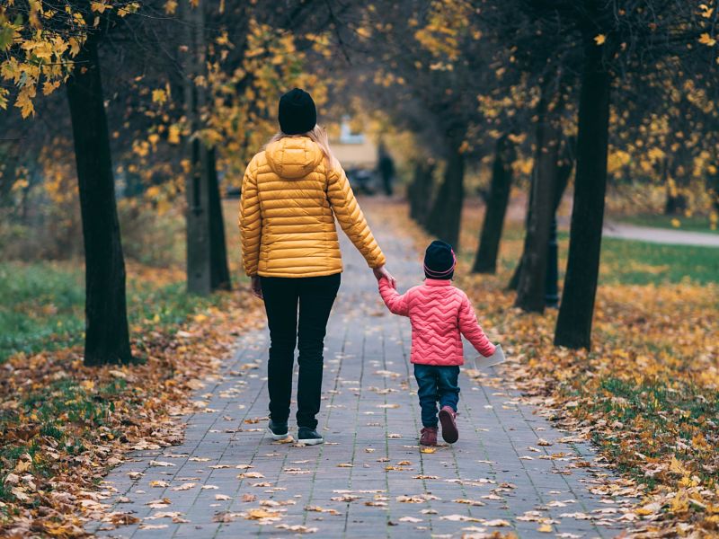 Mum and toddler son take a walk through an autumn park